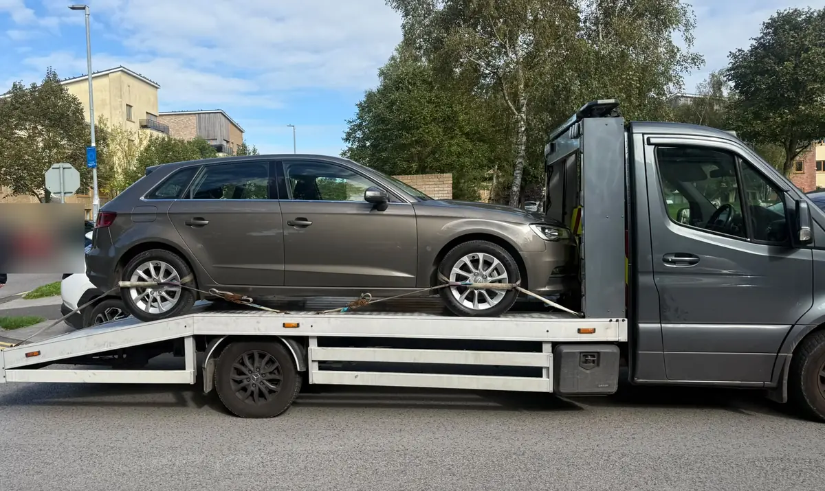A grey hatchback secured on a flatbed tow truck on a Dublin street, car recovery