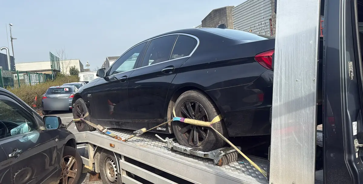 A black saloon car wheel-strapped on a flatbed during vehicle recovery in Dublin