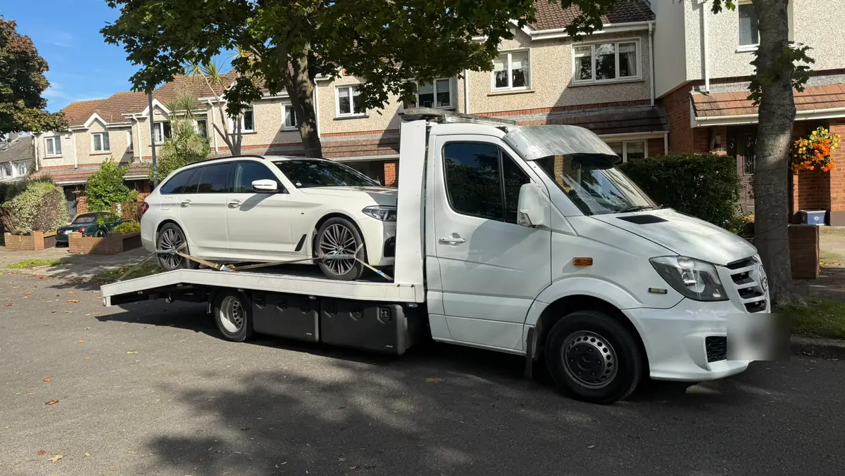 A white flatbed tow truck with an estate car on board on a Dublin housing estate street