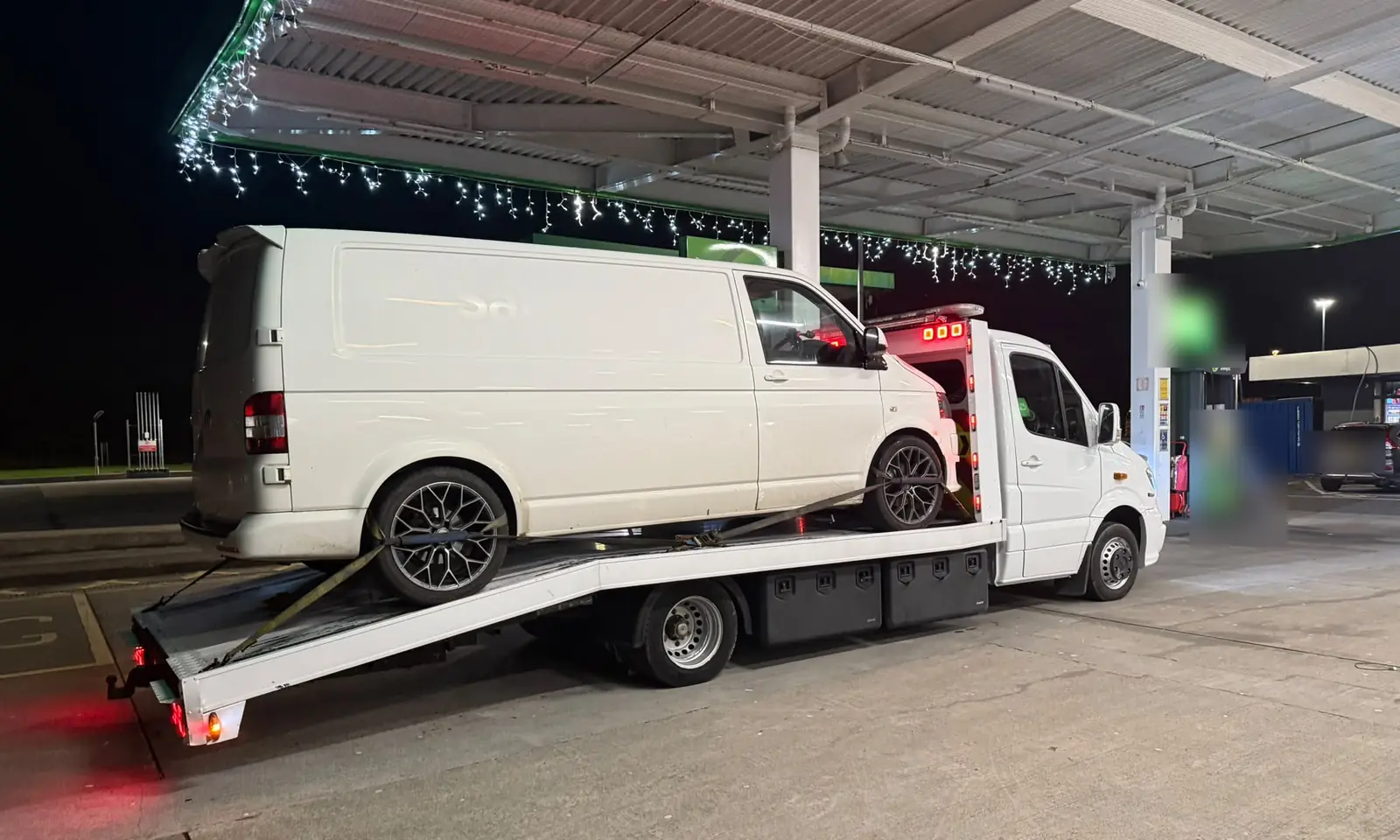 Van towing in Dublin at night: a white van loaded on a flatbed tow truck at a petrol station