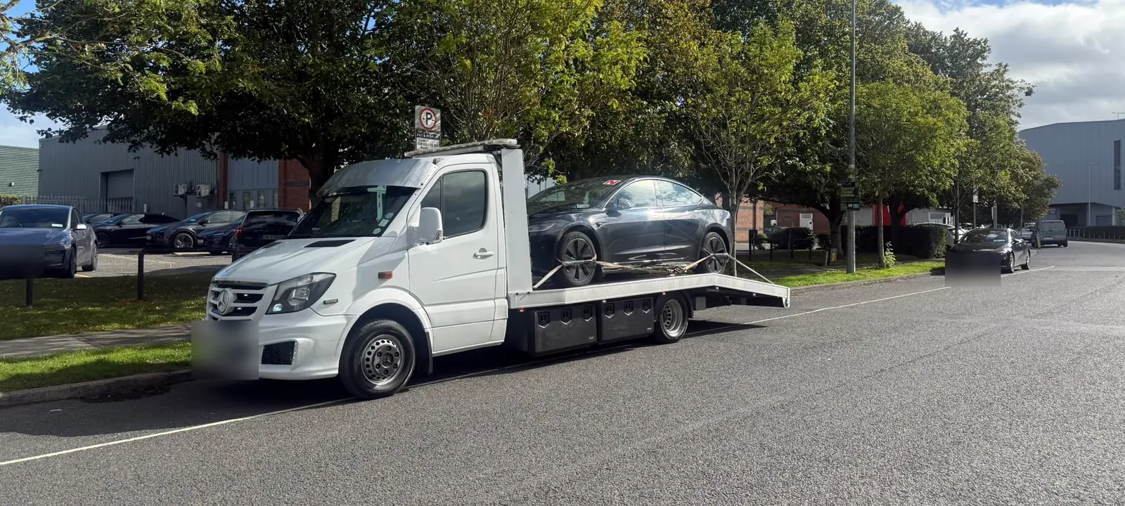 A white flatbed tow truck carrying an electric car along a Dublin industrial estate road
