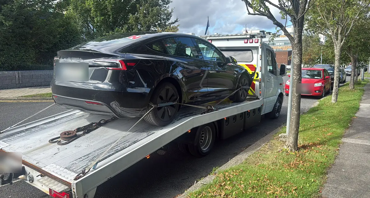 Electric car strapped down on a flatbed tow truck on a tree-lined Dublin street, EV towing