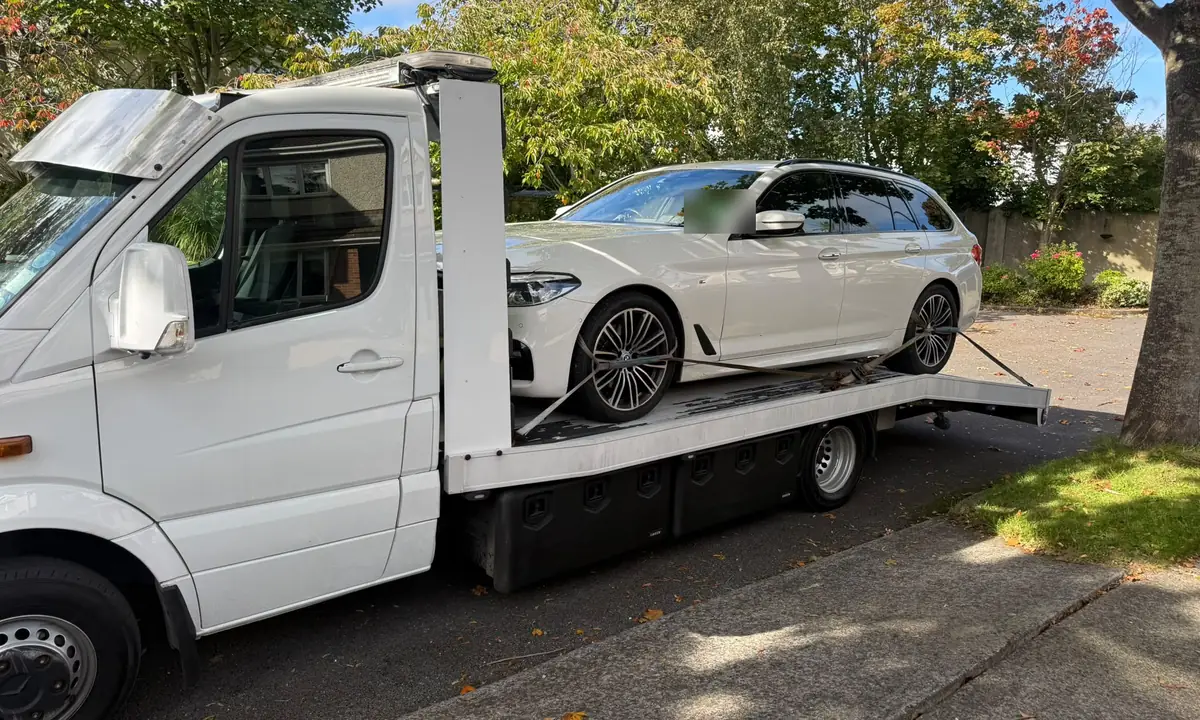 A white estate car loaded on a car recovery truck parked under trees in Dublin