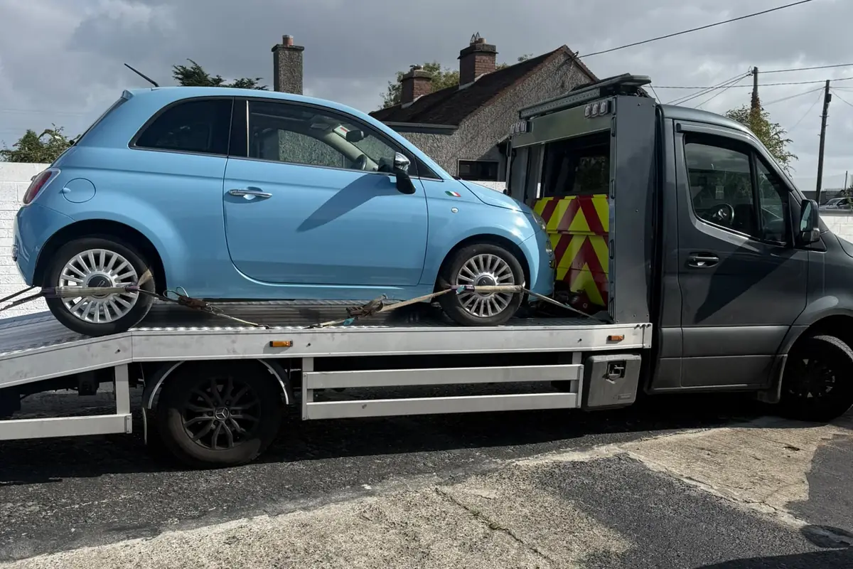 A small blue city car strapped onto a flatbed tow truck for car recovery in Dublin