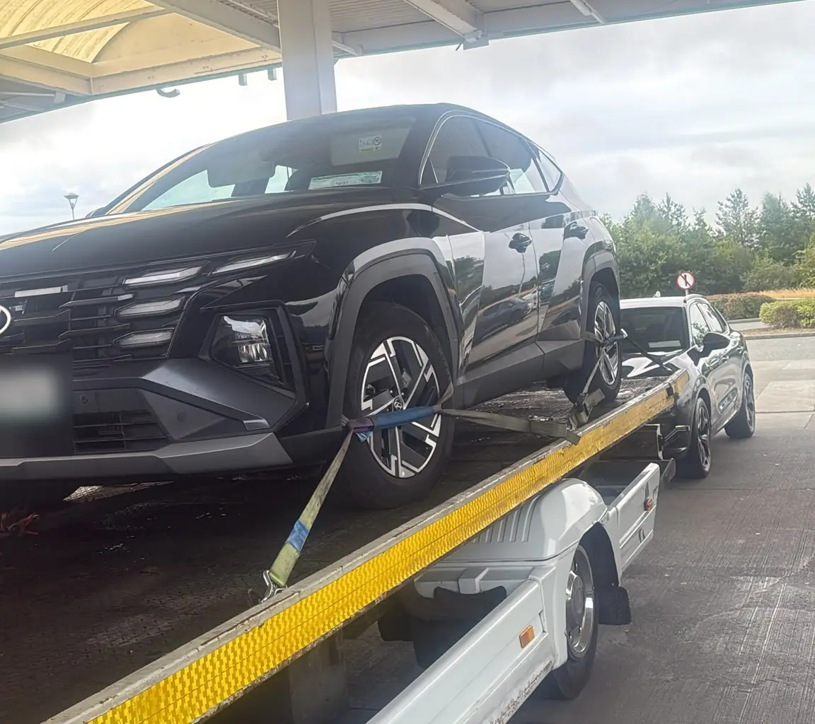 A black SUV secured with wheel straps on a recovery truck under a forecourt canopy in Dublin