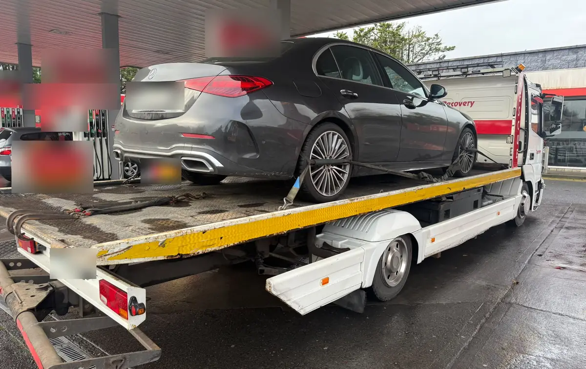 A saloon car on the back of a flatbed tow truck on a wet forecourt after a breakdown in Dublin