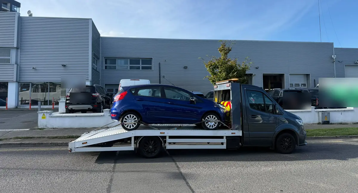 A blue hatchback loaded on a flatbed tow truck with the ramp lowered, car recovery in Dublin