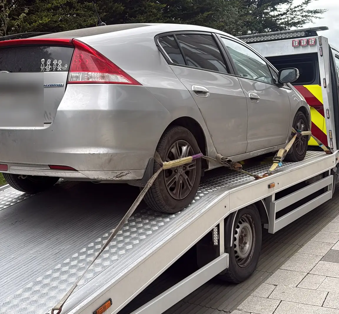 A silver hybrid hatchback strapped onto a flatbed tow truck for car recovery in Dublin
