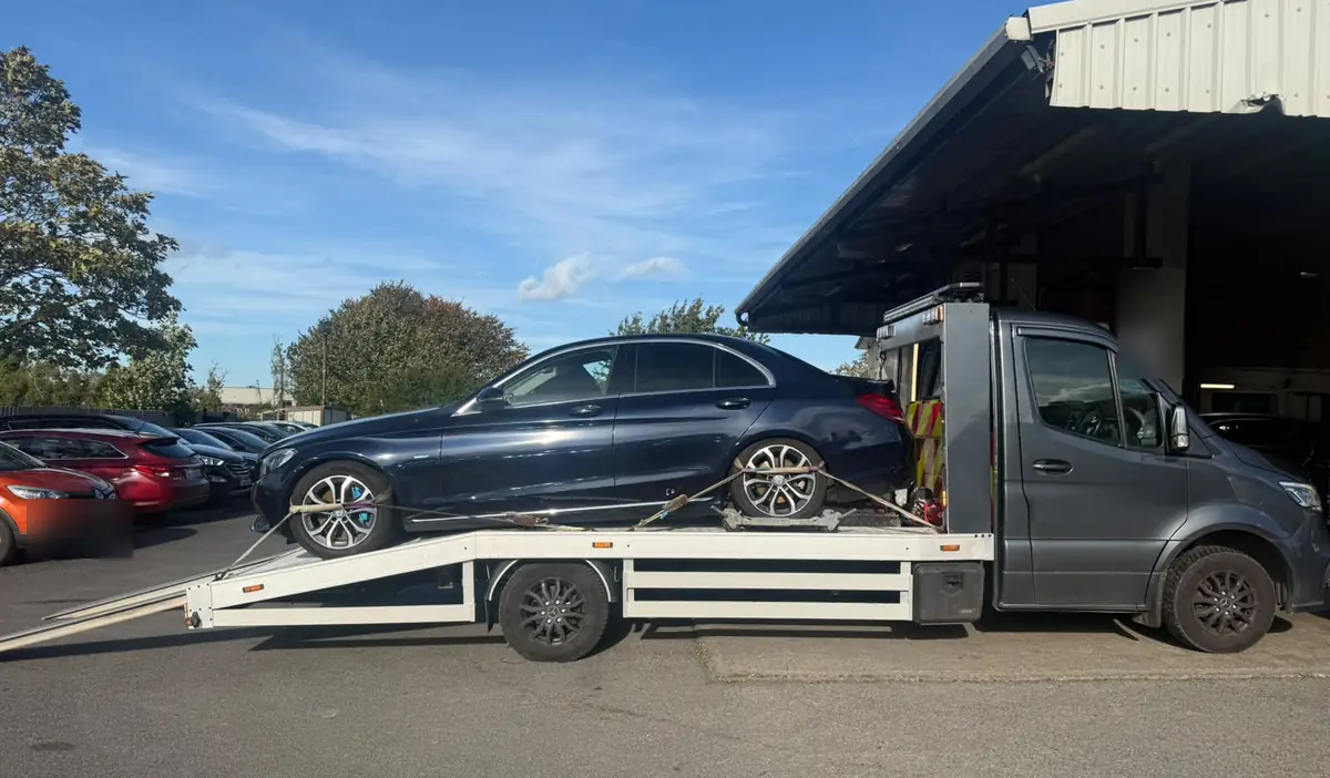 A dark saloon car secured on a flatbed tow truck outside a garage, car towing in Dublin