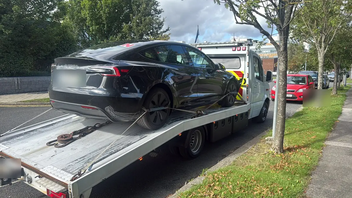 A black electric car secured on the tilted deck of a recovery truck