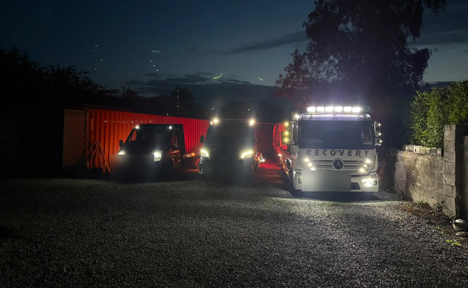 Recovery CC tow trucks lined up at night in Dublin with headlights and roof lights on
