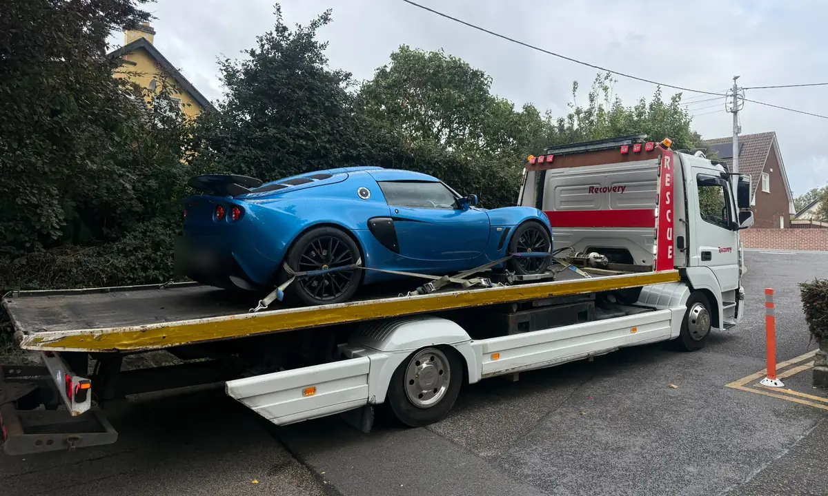 A blue sports car strapped onto the flatbed of a Recovery CC truck