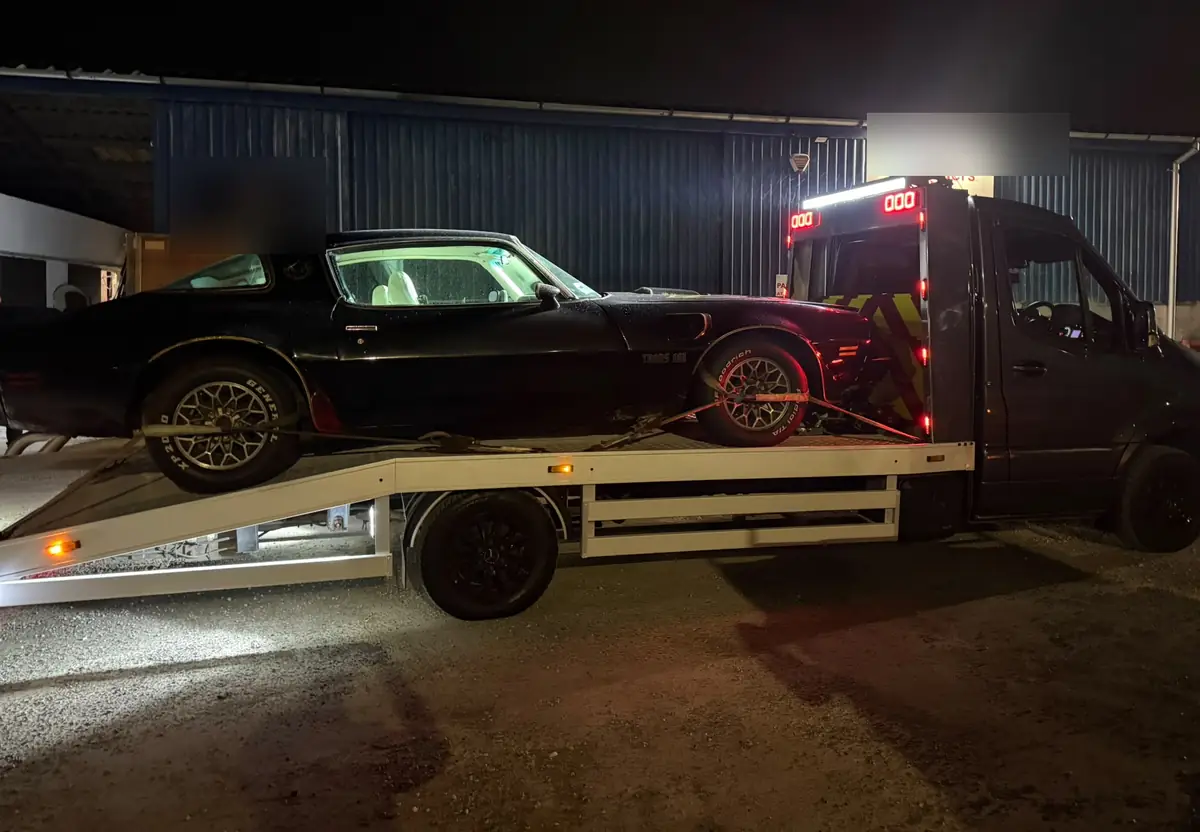 A recovery truck loading a black car at night under bright work lights