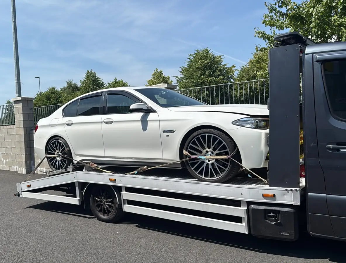 A white saloon car strapped down on the flatbed of a recovery truck beside a Dublin footpath