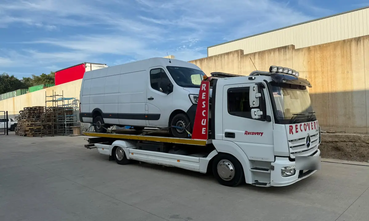 A large white panel van loaded on a Recovery CC truck in a yard